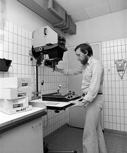 880101 Portret van D. Sleurink, fotograaf van de Gemeentelijke Fotodienst, bij de vergroter in de donkere kamer van de ...